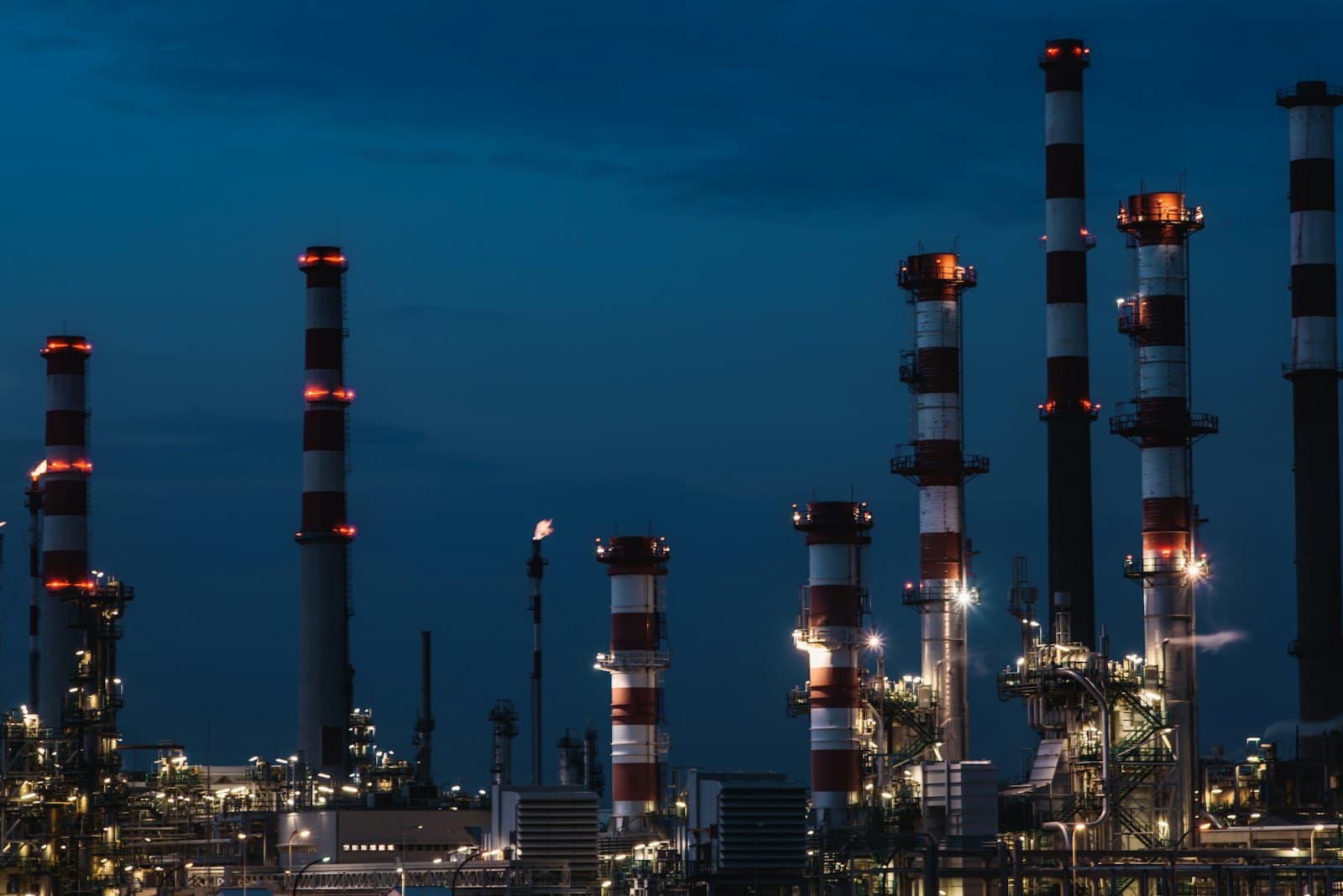 Refineria petrolera iluminada al anochecer con torres de proceso